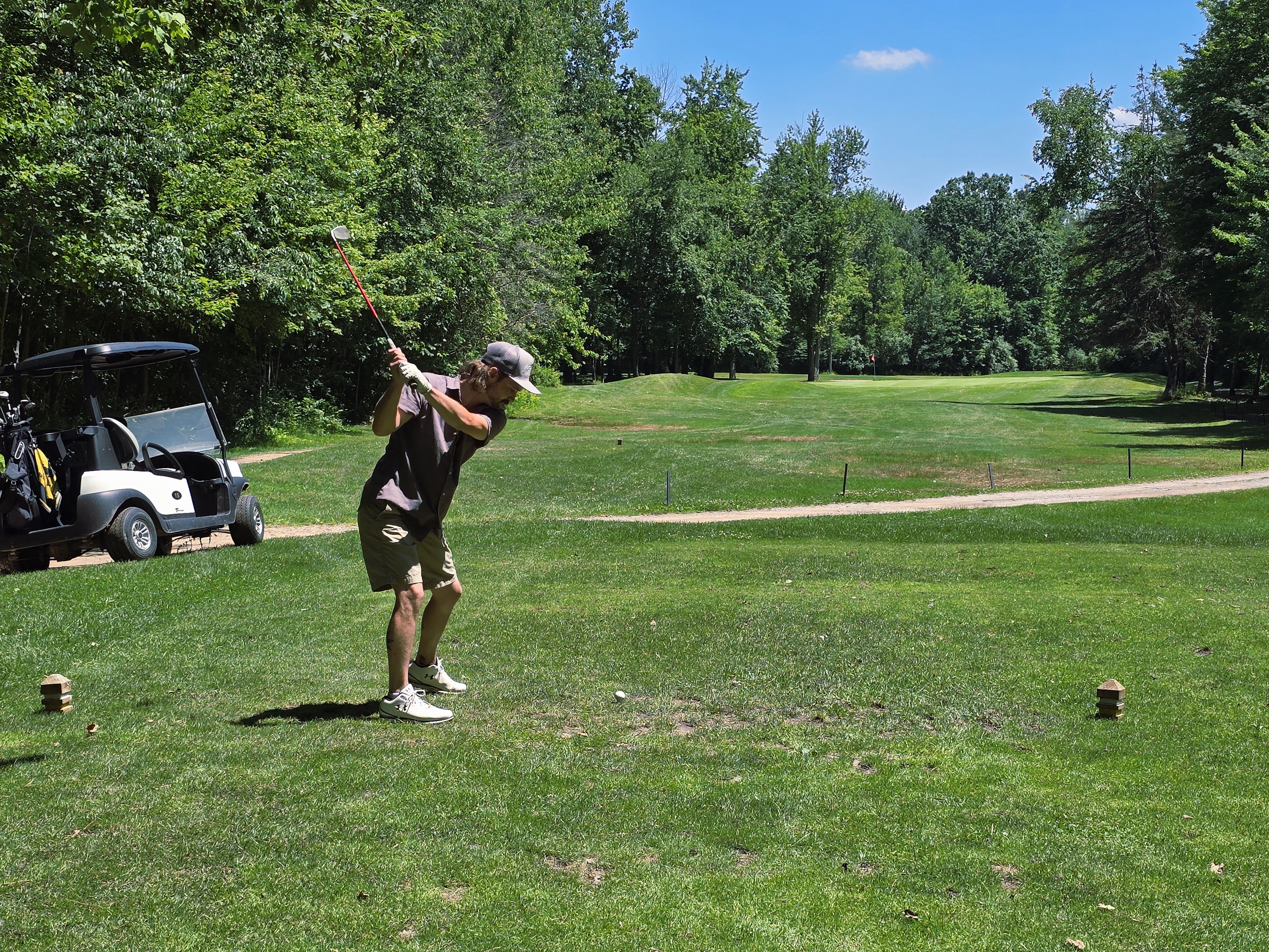 View of golfer on golf course with golf cart near cart path